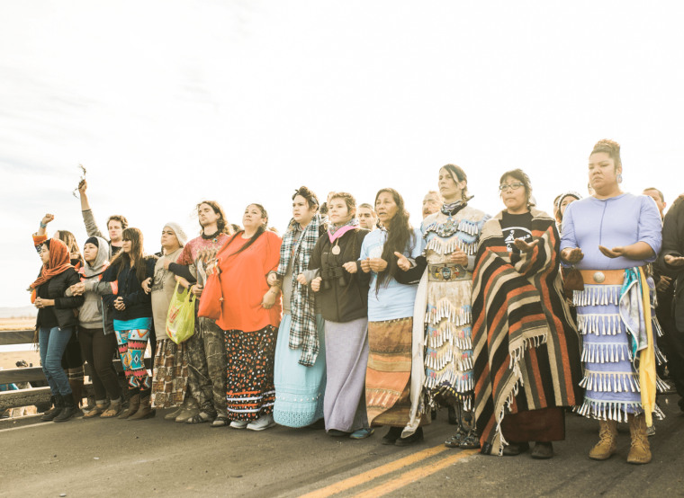 A group of Native people standing in a line with their arms locked together.