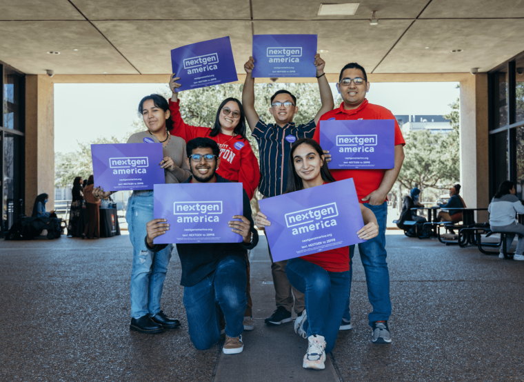 Six people posing for a photo, smiling, while holding purple signs that say Next Gen America.